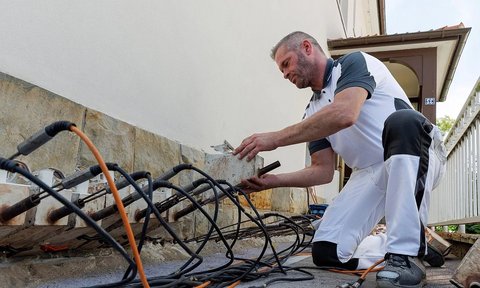 Arbeiter prüft verkabelte Metallstangen an Hauswand